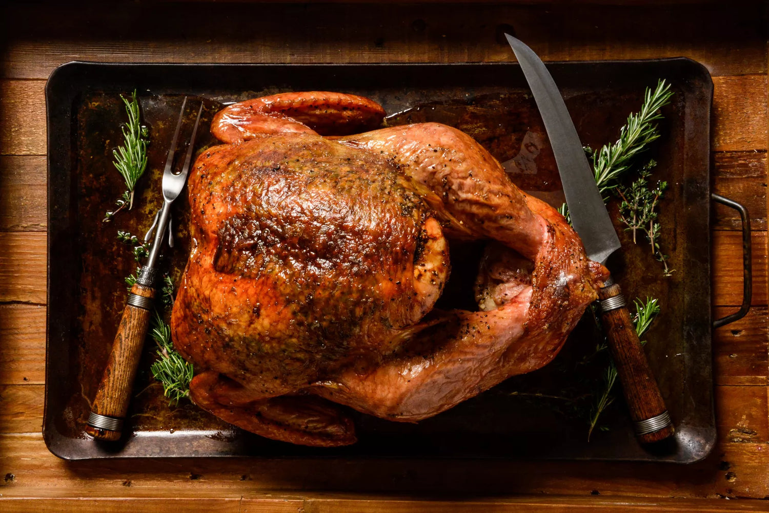 Roasted turkey on a baking tray with utensils on a wooden surface