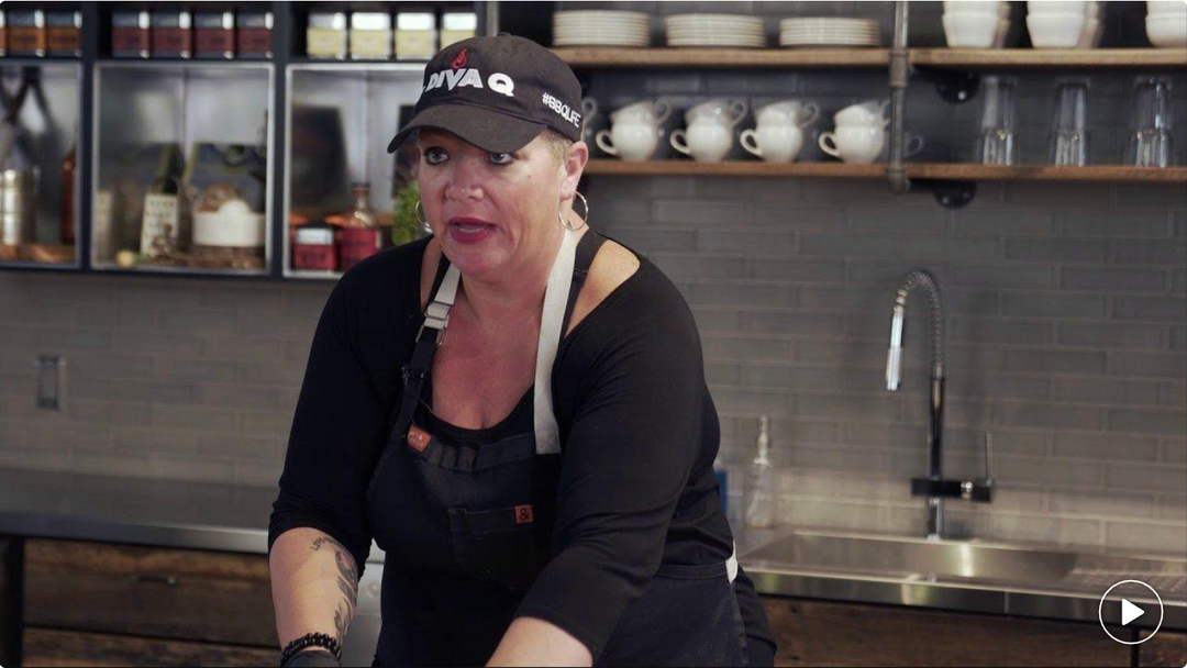 Person wearing a black apron and cap in a kitchen setting