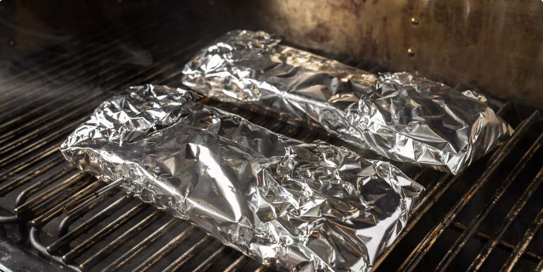 Aluminum foil packets on a grill with smoke