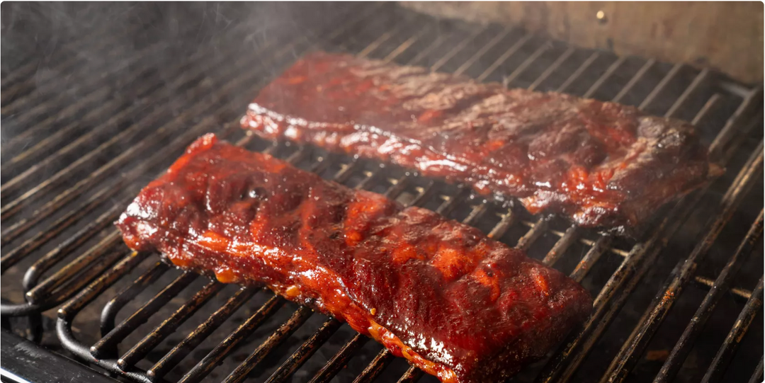 Two pieces of marinated meat on a traeger grill with smoke rising.