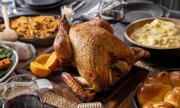 Roasted turkey on a wooden cutting board with side dishes and glasses of red wine on a table.