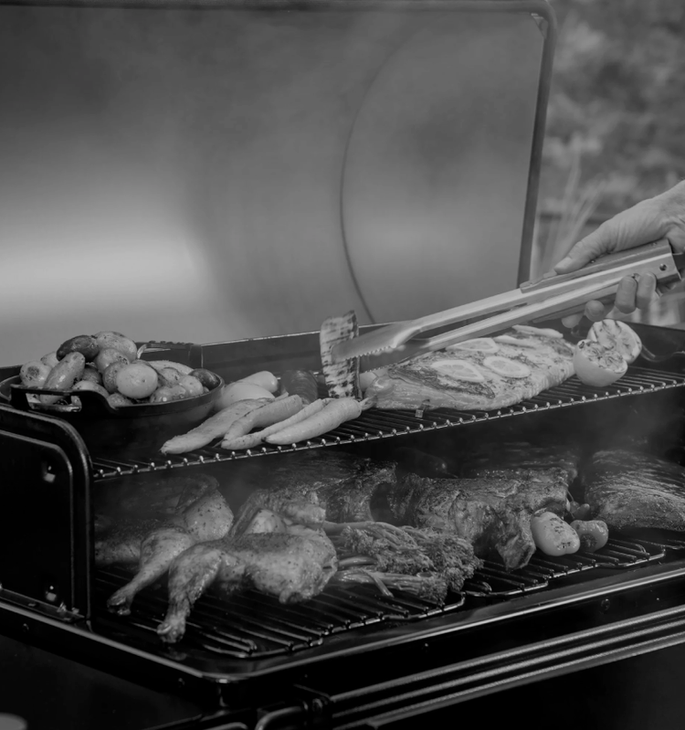 Person grilling meat and vegetables on a traeger grills using tongs.